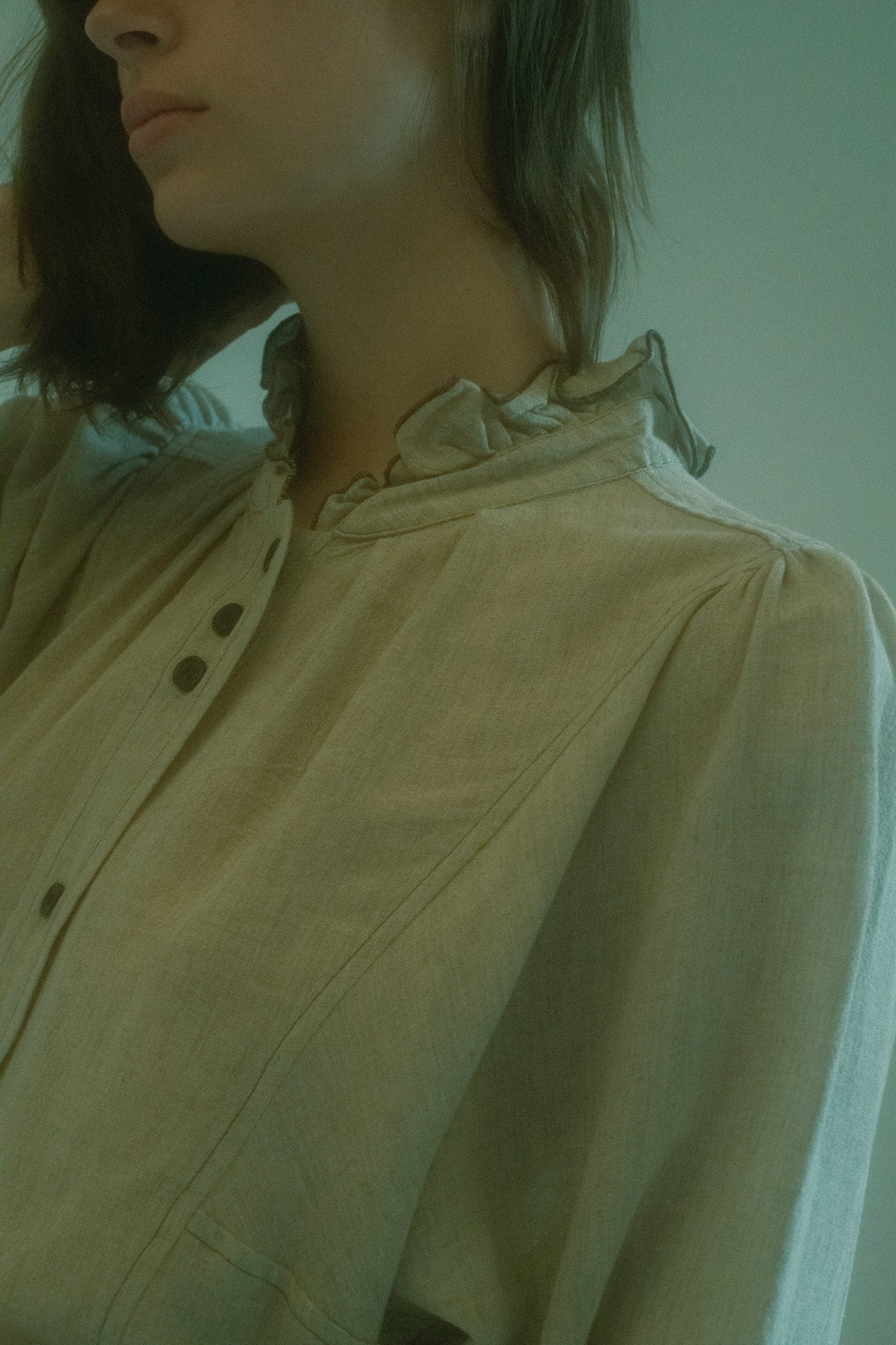 Button details along the front placket and sleeves add subtle refinement, while pleating at the sleeves introduces dynamic texture and movement—perfectly blending structure with soft elegance.