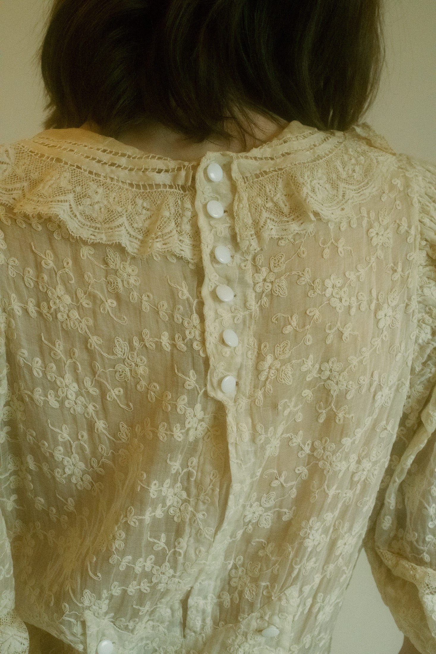 The intricate button closure at the back brings a touch of mystery and refinement, perfectly complementing the ruffle detail at the collar—an exquisite nod to classic femininity.
