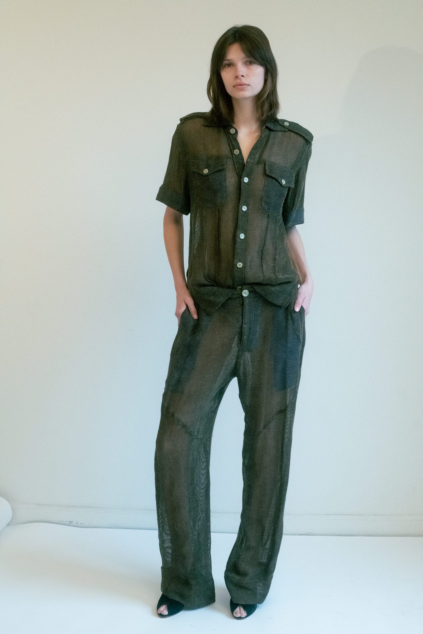The double chest pockets and shoulder tabs suggest strength and utility, but the sheer fabric unveils a world of intrigue—shifting from deep brown to olive green with every change in the light, as though it’s holding its secrets close.