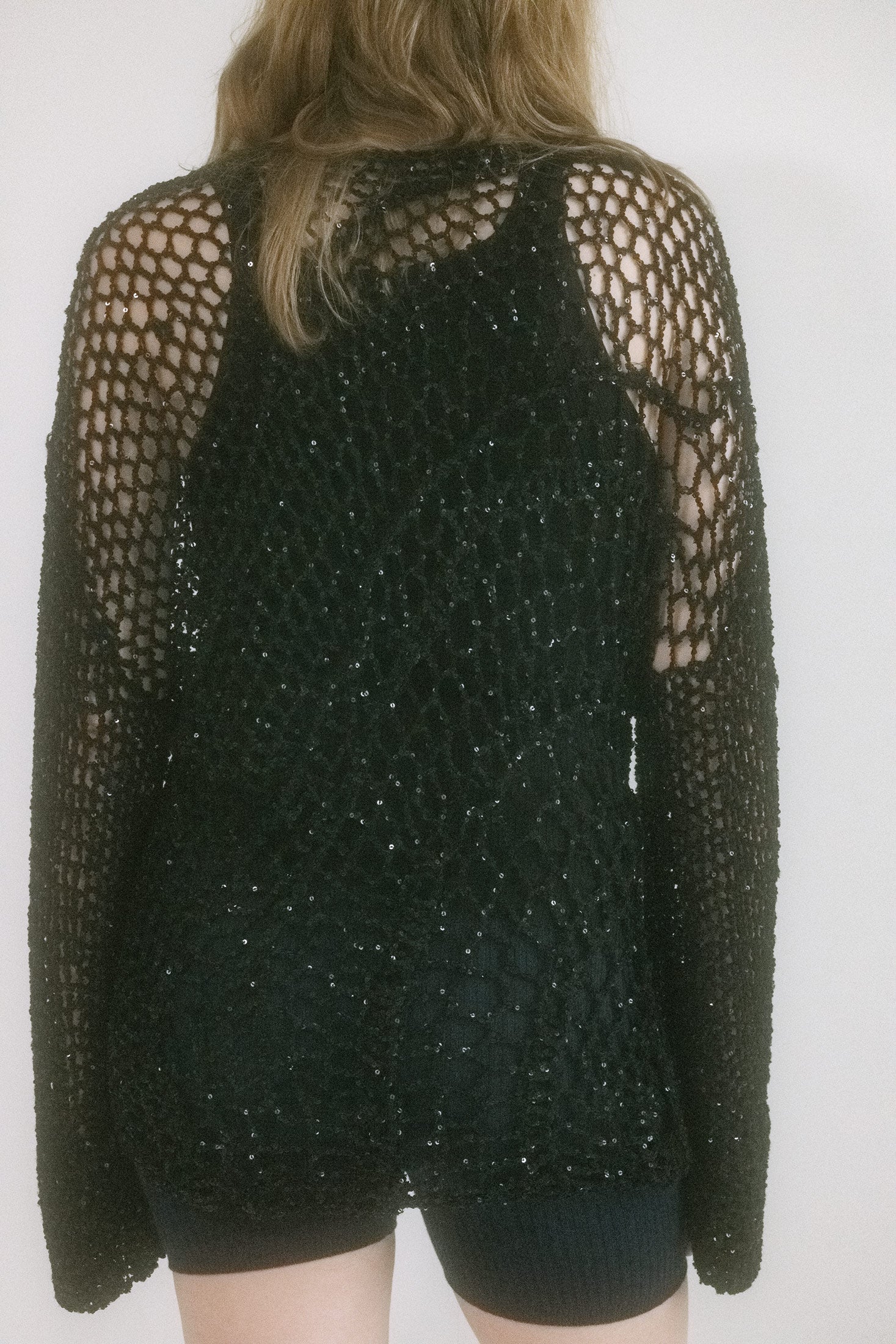 The black knit veils the skin like a whispered secret, while the high neck and relaxed fit add restraint just begging to be undone.
