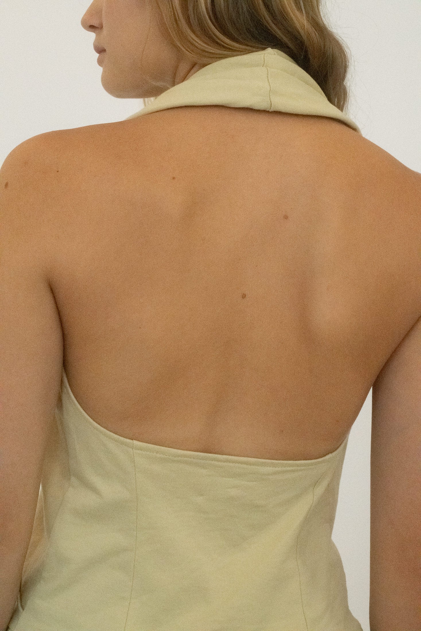 The open back keeps the silhouette light, while a ruffled hem flutters with a playful, off kilter charm.