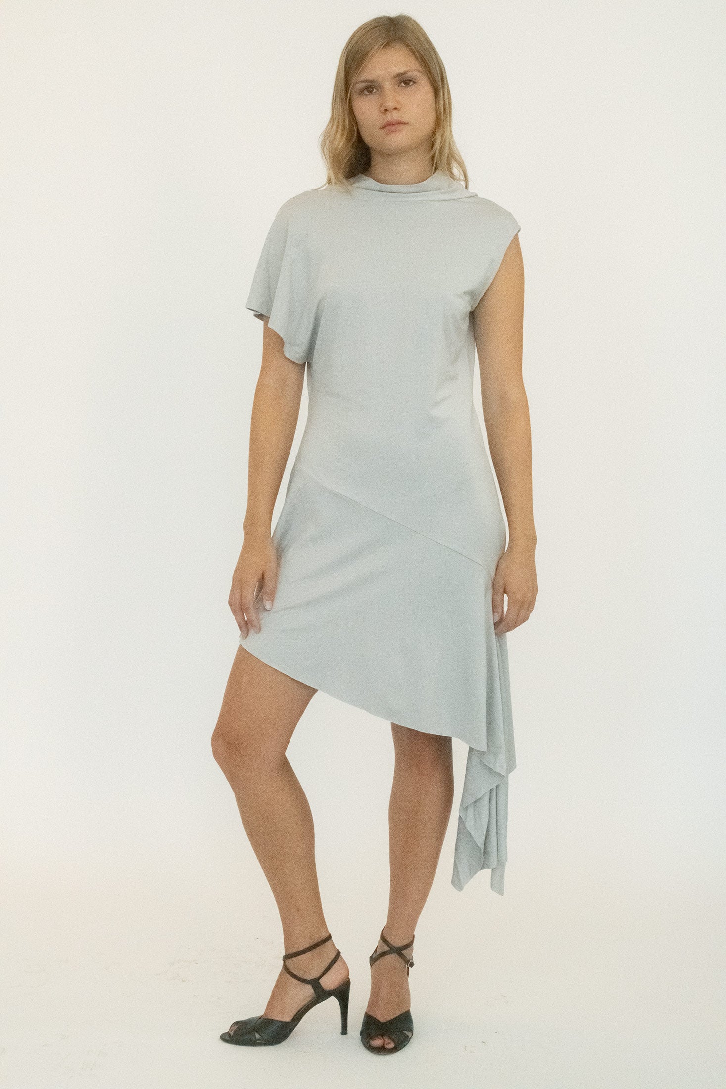 Cut with a mock neckline, it frames the face in clean simplicity before breaking the line with an asymmetrical waterfall shoulder.
