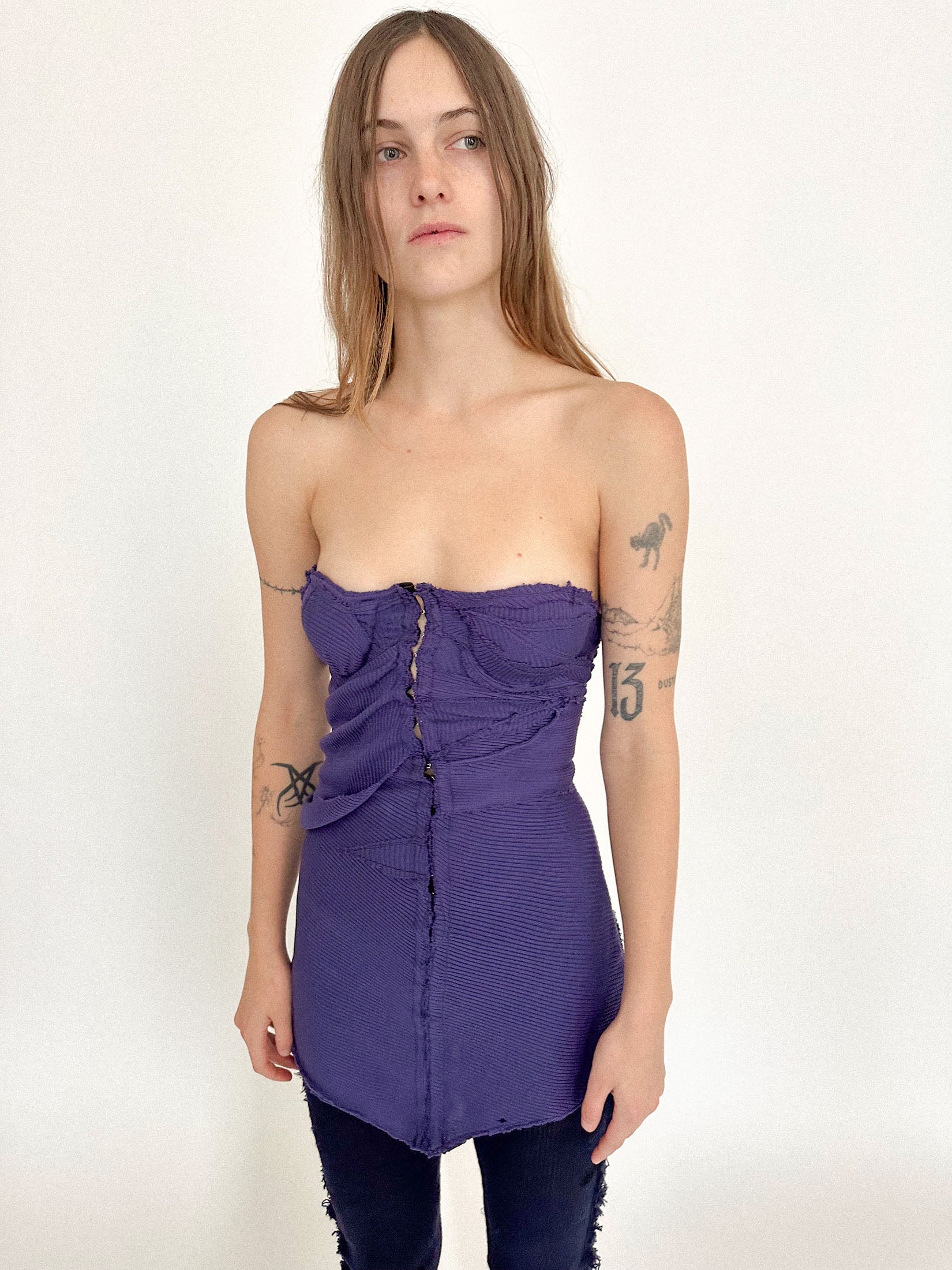 Padded cups and hook-and-eye closures climb the front, giving the knit structure a corseted discipline.