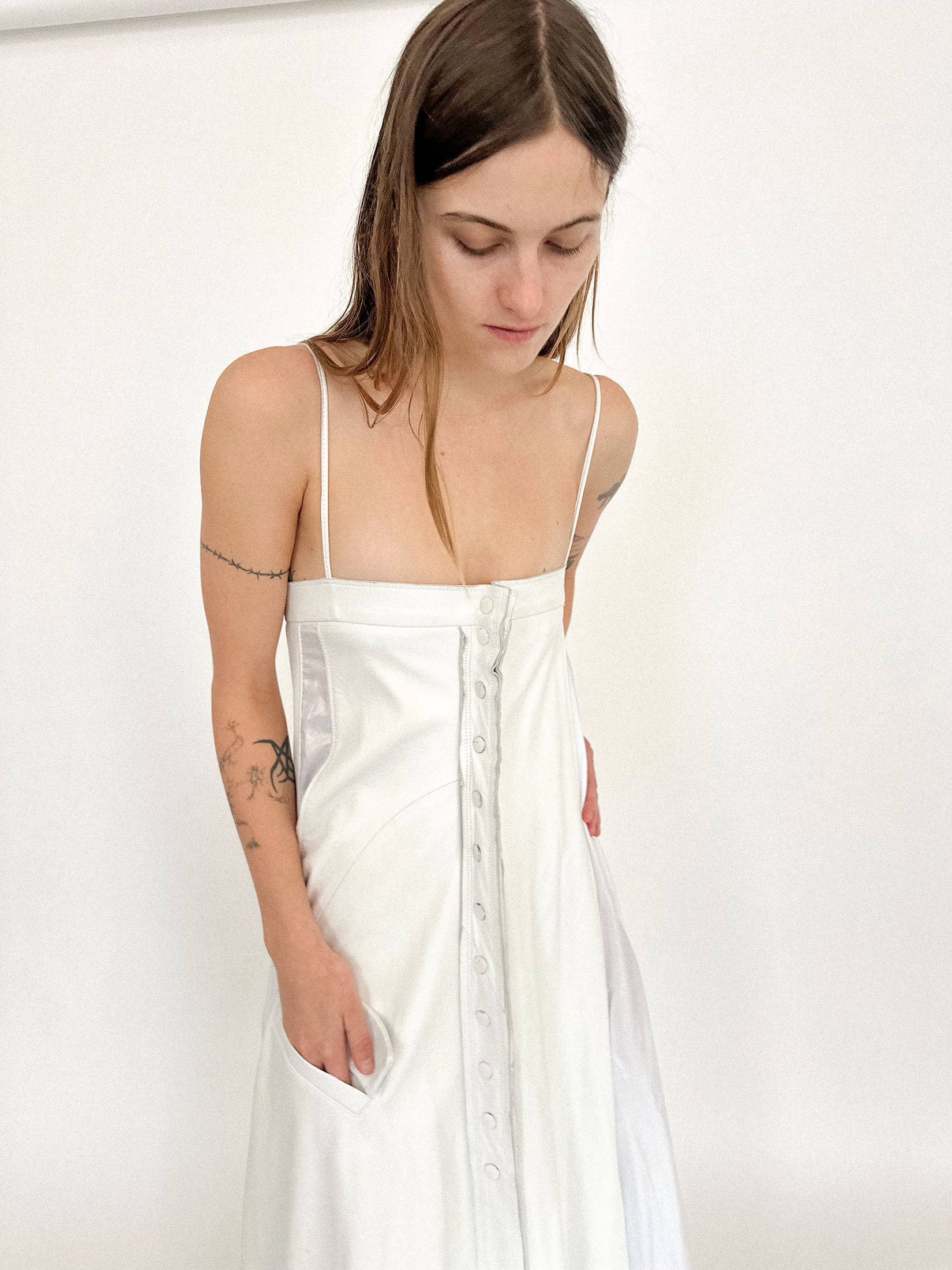 Snaps run down the front, clean and deliberate, while the straight neckline and thin straps keep the gesture minimal, almost architectural.