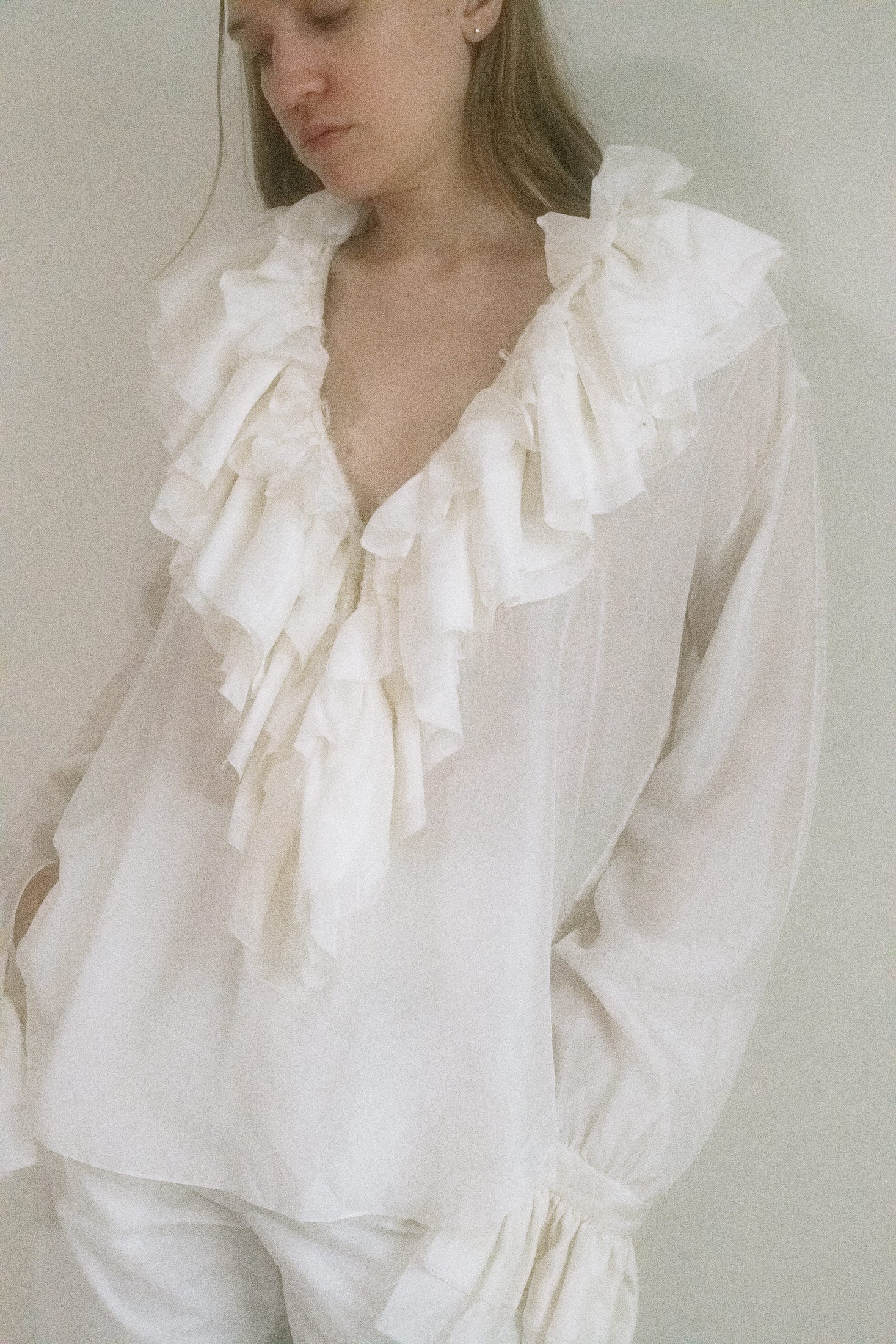 Cut from airy white fabric, it features a plunging V-neck framed by a cascade of ruffles that trail seductively down the front. 
