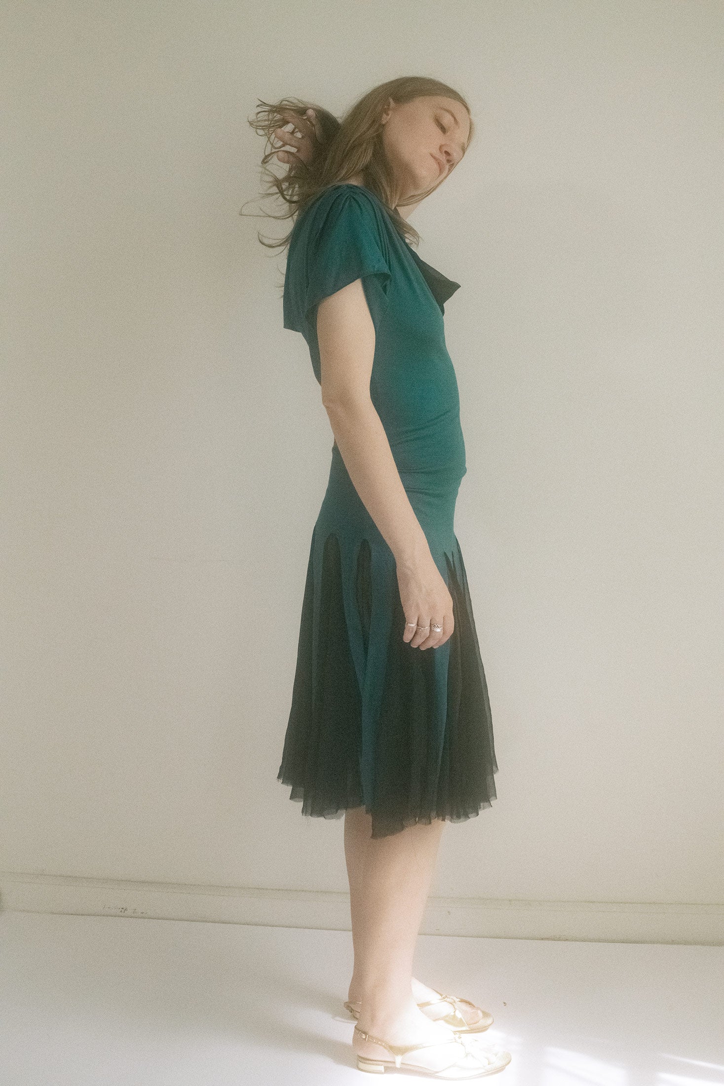 Panels of sheer chiffon flicker at the skirt and neckline, catching light—and suspicion. 
