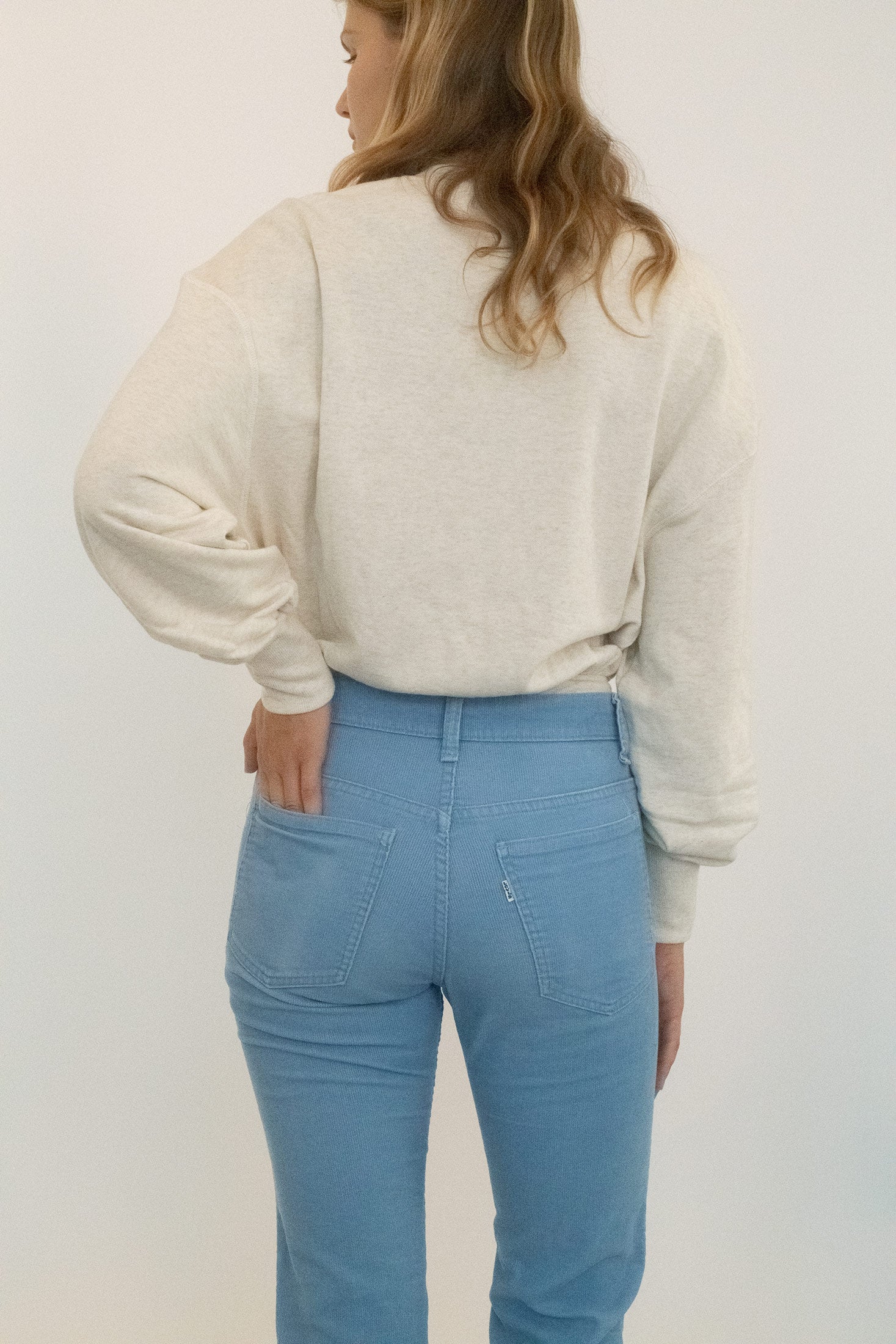 The crewneck frames the collarbone in quiet simplicity, while the fit drapes loose before cinching neatly at the waist, a casual gesture that still reads like control.