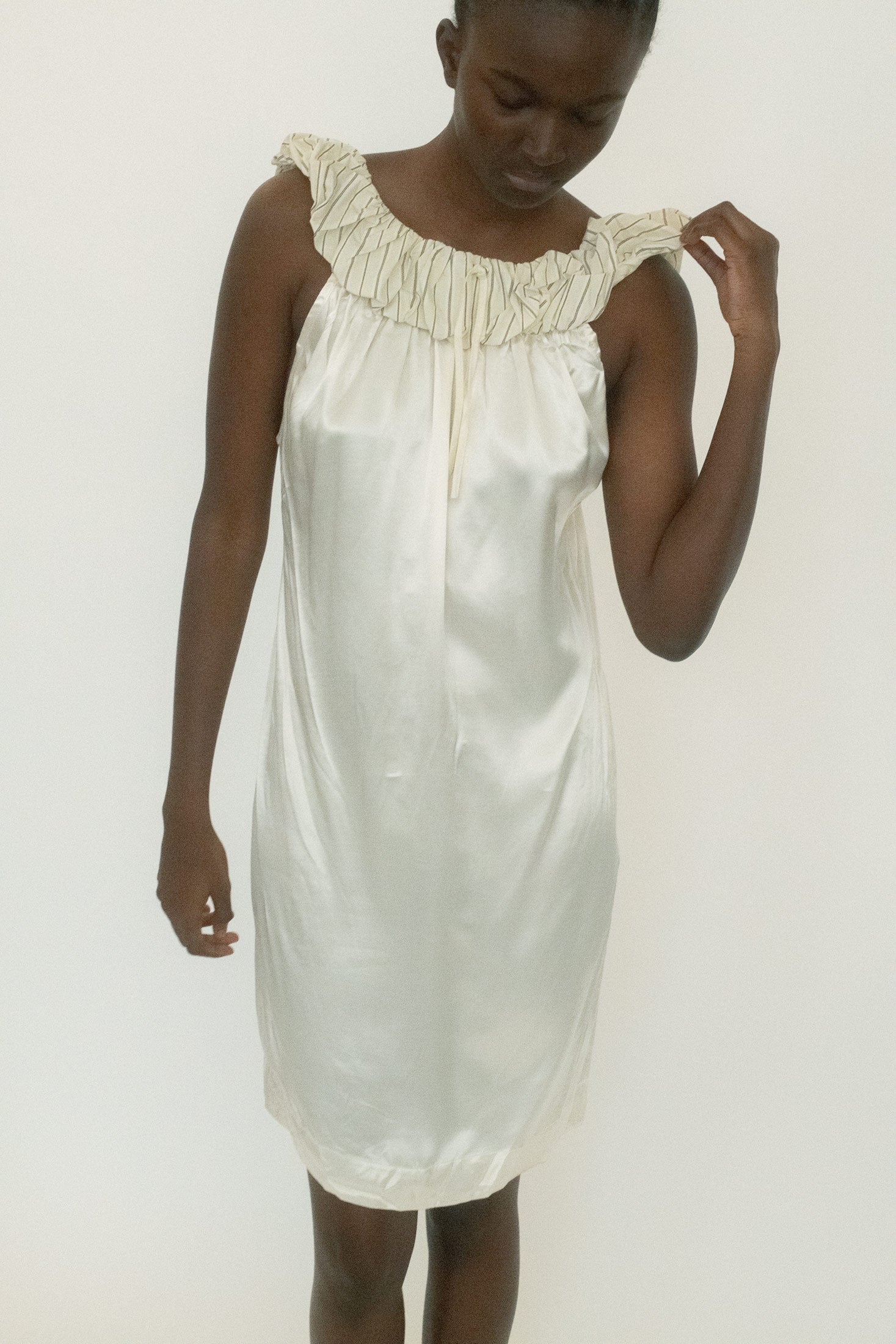 At the neckline, a voluminous pinstriped collar gathers into a cinched drawstring detail, dramatic but precise.